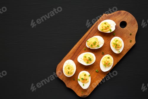 Preview: Homemade Deviled Eggs With Chives On A Rustic Wooden Board On A Black Background, Top View. Flat