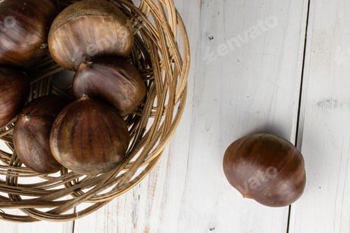 Preview: Group Of Seven Whole Edible Brown Chestnut In Round Rattan Bowl Flatlay On White Wood