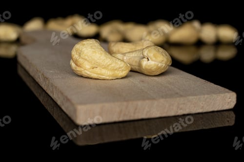 Preview: Lot Of Whole Brown Nut Cashew Two In Focus On Wooden Cutting Board Isolated On Black Glass