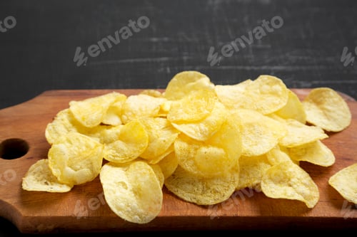 Preview: Crispy Potato Chips With Salt On A Rustic Wooden Board On A Black Surface, Low Angle View. Copy