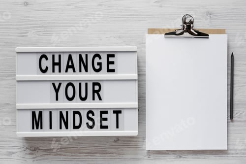 Preview: 'Change Your Mindset' Words On A Lightbox, Clipboard With Blank Sheet Of Paper On A White Wooden