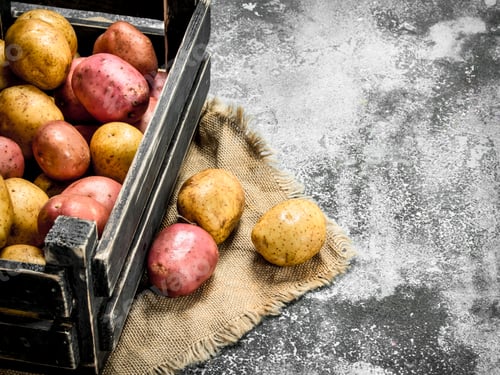 Preview: Fresh Potatoes In A Box. On A Rustic Background.