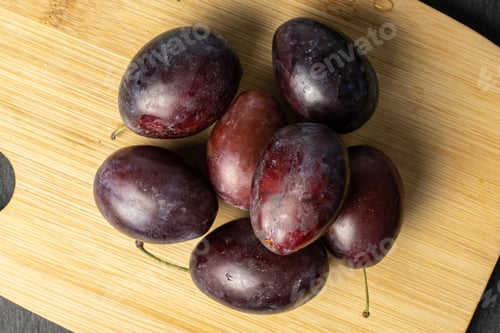 Preview: Group Of Seven Whole Sweet Purple Plum On Bamboo Cutting Board Flatlay On Grey Stone