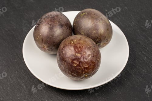 Preview: Group Of Three Whole Sweet Dark Purple Passion Fruit On White Ceramic Plate On Grey Stone