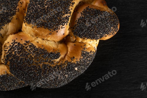 Preview: Closeup Of One Whole Twisted Poppy Seed Bun Flatlay On Grey Stone