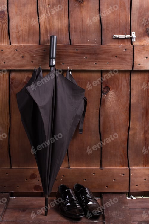 Preview: Black Male Umbrella And Classic Patent Leather Shoes Near Wooden Fence.