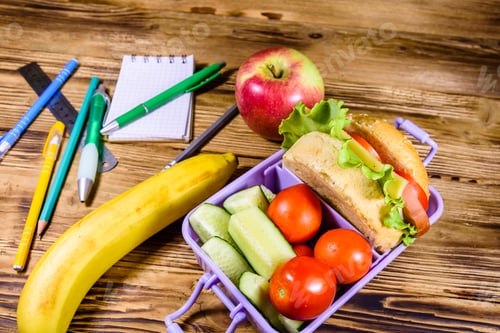 Preview: Ripe Apple, Banana, Different Stationeries And Lunch Box With Hamburger, Cucumbers And Tomatoes On