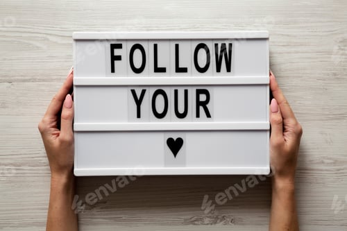 Preview: Female Hands Hold Modern Board With Text 'Follow You Heart' Over White Wooden Background. Closeup.