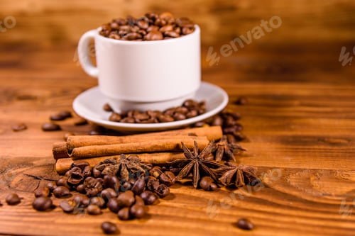 Preview: White Cup Filled With Coffee Beans, Star Anise And Cinnamon Sticks On Rustic Wooden Table