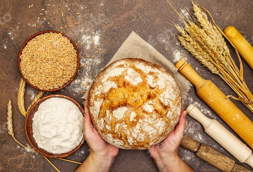 Preview: Female Hands Hold Freshly Baked Bread. Wheat Ears, Wooden Rolling Pins And A Bowls Of Flour And