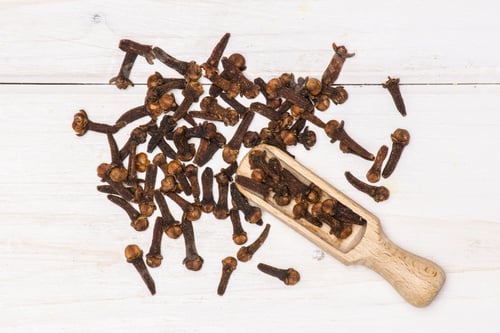 Preview: Lot Of Whole Small Dried Cloves Spice With Wooden Scoop Flatlay On White Wood