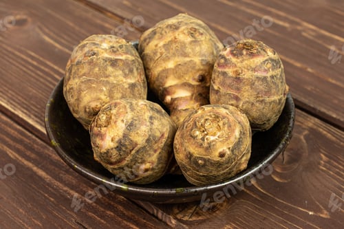 Preview: Group Of Five Whole Fresh Brown Jerusalem Artichoke In Dark Ceramic Bowl On Brown Wood