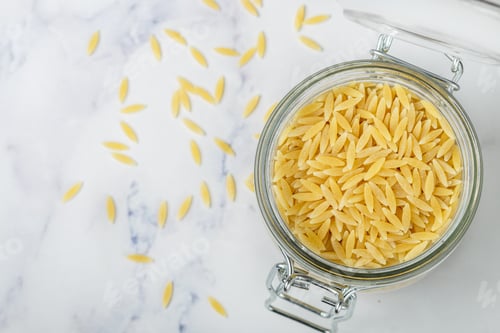 Preview: Orzo, A Form Of Pasta Shaped Like Rice In A Glass Jar On A Marble Surface. Selective Focus, Copy