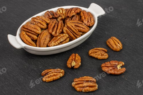 Preview: Lot Of Whole Dry Brown Pecan Nut In White Oval Ceramic Bowl On Grey Stone