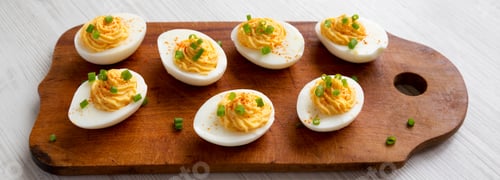 Preview: Homemade Deviled Eggs With Chives On A Rustic Wooden Board On A White Wooden Background, Low Angle