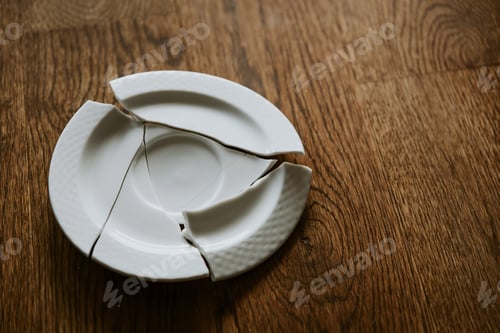Preview: Broken White Porcelain Plate On Wooden Floor. Top View Of Damaged Ceramic Empty Plate, Split In