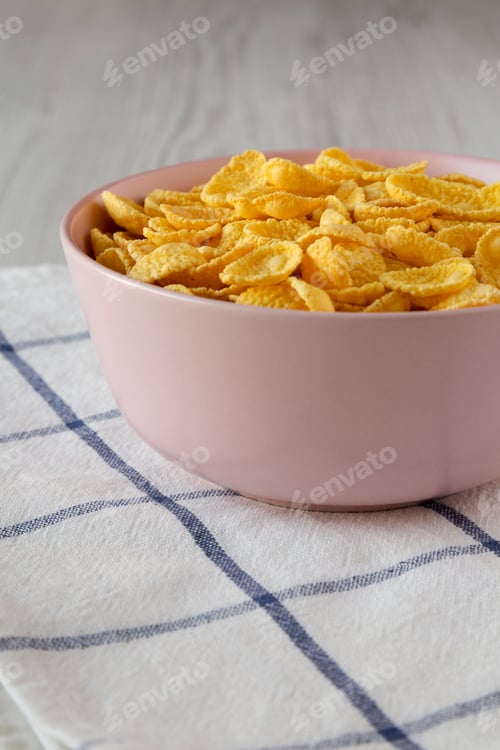 Preview: Corn Flakes In A Pink Bowl For Breakfast Over White Wooden Surface, Side View.