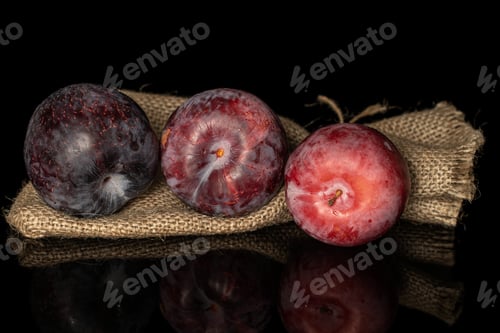Preview: Group Of Three Whole Fresh Red Plum With Jute Bag Isolated On Black Glass