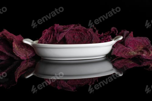 Preview: Lot Of Slices Of Dried Red Beetroot In White Oval Ceramic Bowl Isolated On Black Glass