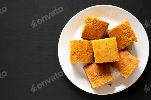 Preview: Homemade Sliced Cornbread Ready To Eat On A White Plate On A Black Background, Top View. Flat Lay