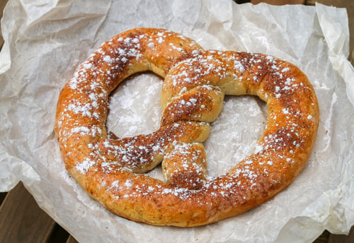 Preview: Cinnamon Sugar Soft Pretzel On A Wooden Table In A Street Cafe. Snack For Tea Or Coffee. Selective