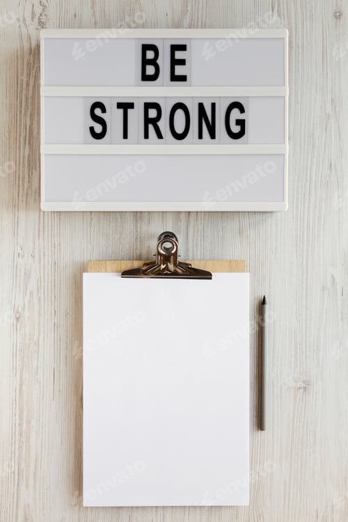 Preview: 'Be Strong' Words On A Lightbox, Noticepad With Blank Sheet Of Paper On A White Wooden Background
