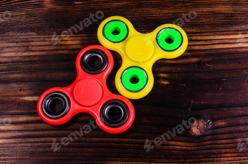Preview: Yellow And Red Fidget Spinners On Rustic Wooden Desk. Top View