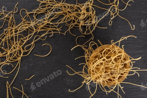 Preview: Lot Of Pieces Of Thin Raw Pasta Noodles In Wooden Bowl Flatlay On Grey Stone