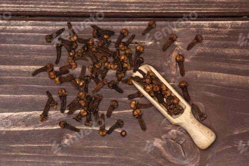 Preview: Lot Of Whole Small Dried Cloves Spice With Wooden Scoop Flatlay On Brown Wood