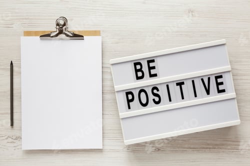 Preview: 'Be Positive' Words On A Modern Board, Clipboard With Blank Sheet Of Paper On A White Wooden