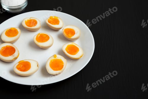 Preview: Homemade Unami Soy Sauce Eggs On A White Plate On A Black Background, Side View. Copy Space.