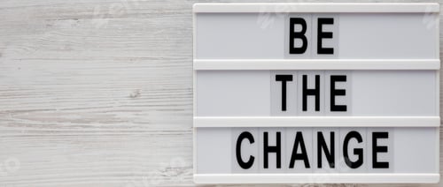 Preview: 'Be The Change' Words On A Modern Board On A White Wooden Surface, Top View. Overhead, From Above