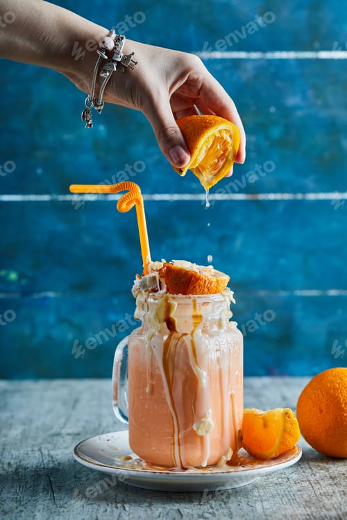 Preview: A Woman Hand Squeezing An Orange In Smoothie And Slice Of Orange On White Plate