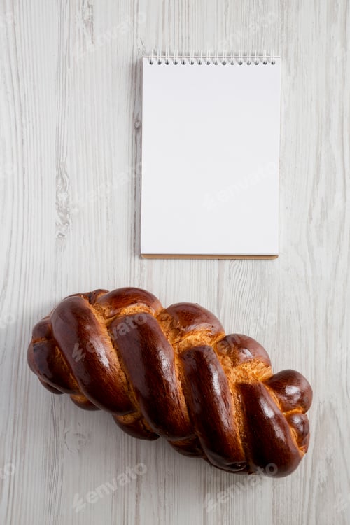 Preview: Homemade Jewish Challah Bread And Blank Notepad On A White Wooden Background, Top View. Copy Space.