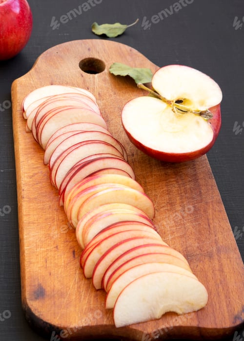 Preview: Slices Of Red Apples On Rustic Wooden Board On Black Surface, Low Angle View. Close-Up.