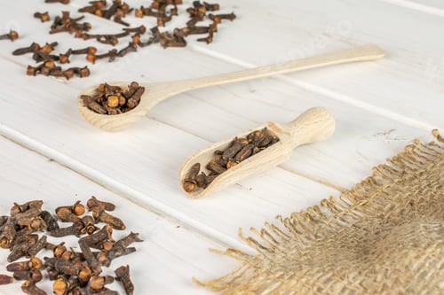Preview: Lot Of Whole Dry Brown Clove In A Wooden Scoop In A Wooden Spoon On Natural Sackcloth On White Wood