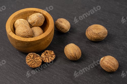 Preview: Group Of Eight Whole One Half One Piece Of Dry Brown Nutmeg In Tiny Wooden Bowl On Grey Stone