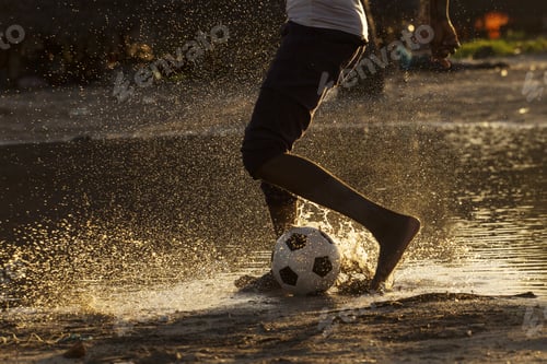 Preview: Legs Of A Black Child Playing Footbal In Water At Sunset