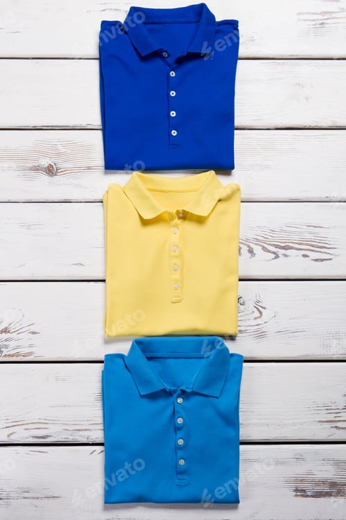 Preview: Blue, Navy And Yellow T-Shirts. Polo Shirts On Wooden Background. Lady'S Colorful Clothing On