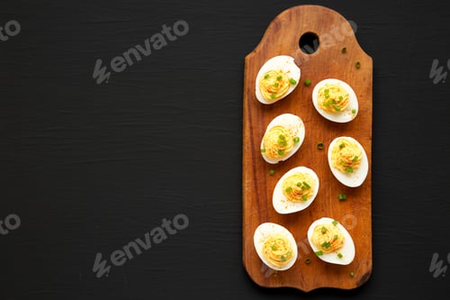Preview: Homemade Deviled Eggs With Chives On A Rustic Wooden Board On A Black Background, Top View. Flat