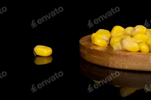 Preview: Lot Of Pieces Of Canned Yellow Corn On Round Bamboo Coaster Isolated On Black Glass