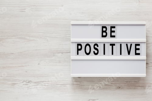 Preview: 'Be Positive' Words On A Lightbox On A White Wooden Background, Top View. Overhead, From Above