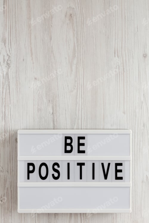 Preview: 'Be Positive' Words On A Lightbox On A White Wooden Surface, Top View. Overhead, From Above, Flat