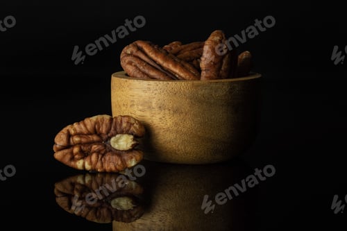Preview: Lot Of Whole Fresh Brown Pecan Nut Half With One Near In A Wooden Bowl Isolated On Black Glass