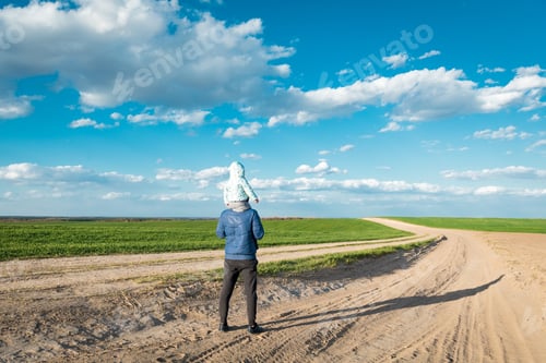 Visualização: Garotinho está sentado nos ombros do pai e apontando para o sol no campo durante a bela
