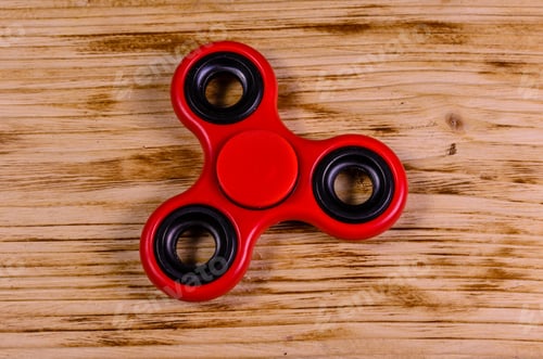 Preview: Red Fidget Spinner On Rustic Wooden Desk. Top View
