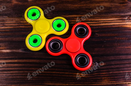 Preview: Yellow And Red Fidget Spinners On Rustic Wooden Desk. Top View