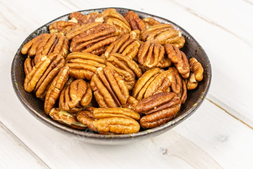 Preview: Lot Of Whole Dry Brown Pecan Nut In Dark Ceramic Bowl On White Wood