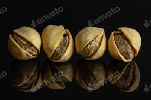 Preview: Group Of Four Whole Ripe Green Pistachio In Closeup In Row Isolated On Black Glass