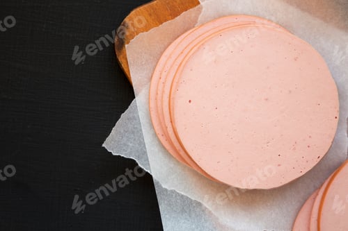 Preview: Sliced Pork Bolgna Meat On A Rustic Wooden Board On A Black Surface, Top View. Flat Lay, Overhead